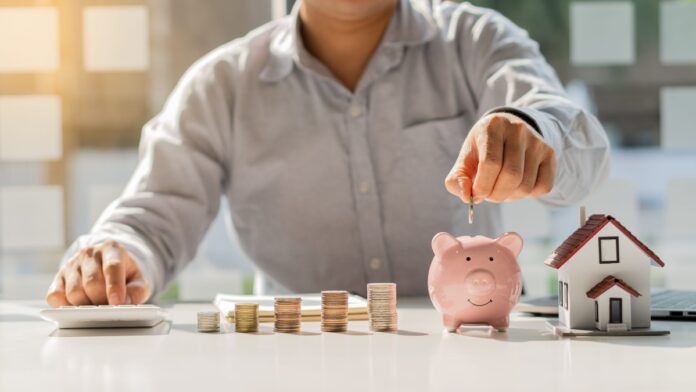 A businessman puts coins in a piggy bank as savings for paying for a house.